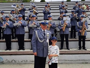 na zdjęciu widać ustawionych na stopniach członków policyjnej orkiestry, policjanci trzymają w rękach instrumenty muzyczne, na pierwszym planie policjant pozuje do wspólnego zdjęcia z chłopcem