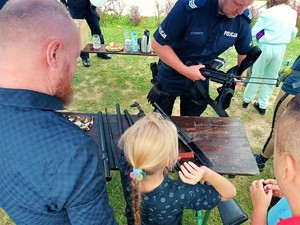policjant prezentuje jednostkę broni, obserwuje to mężczyzna i dziewczynka