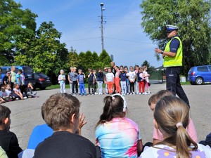 policjant prowadzi spotkanie profilaktyczne z dziećmi, dzieci stoją na boisku szkolnym przodem do policjanta