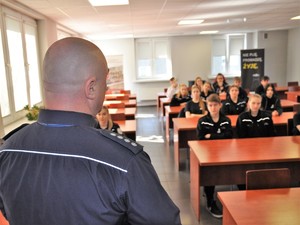 policjant stoi przed uczniami klasy mundurowej siedzącymi w sali