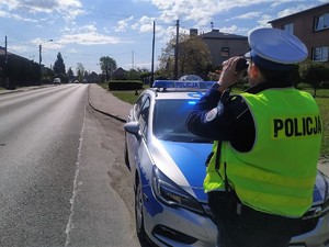 policjant stoi przed radiowozem, przez lornetkę obserwuje pojazdy