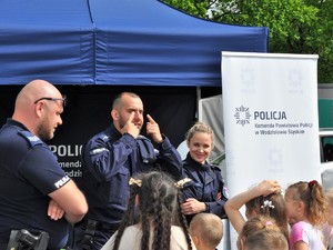 policjant wskazuje palcami na swoje oczy, obok niego stoją policjant i policjantka, przed nimi stoi grupa dzieci